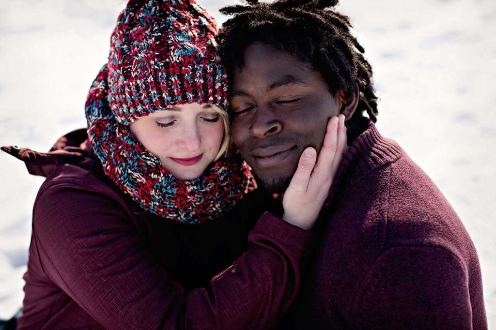 Romantic Winter Engagement Photos of Interracial Couple Sitting on Snow