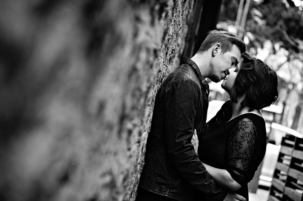 Candid photography of couple sharing a kiss by a wall